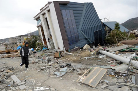 Một người dân Nhật đi qua đống đổ nát và ngôi nhà xiêu vẹo ở thành phố Ofunato,