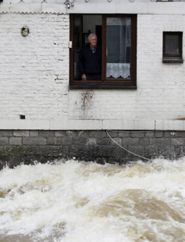 Một người đàn ông ở Bỉ đứng nhìn dòng nước lũ hung dữ tràn qua đường cạnh nhà, con sông Walonie tràn bờ sau mưa lớn.