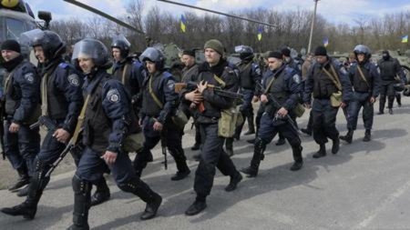Các thành viên của Bộ Nội vụ Ukraina đi qua một máy bay trực thăng MI -8 quân sự và xe bọc thép tại một trạm kiểm soát gần thị trấn Izium , phía đông Ukraine , ngày 15 tháng tư năm 2014 .