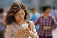 A woman looks at her smartphone as she walks on a busy street in downtown Shanghai, September 25, 2013.