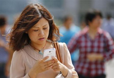 A woman looks at her smartphone as she walks on a busy street in downtown Shanghai, September 25, 2013.