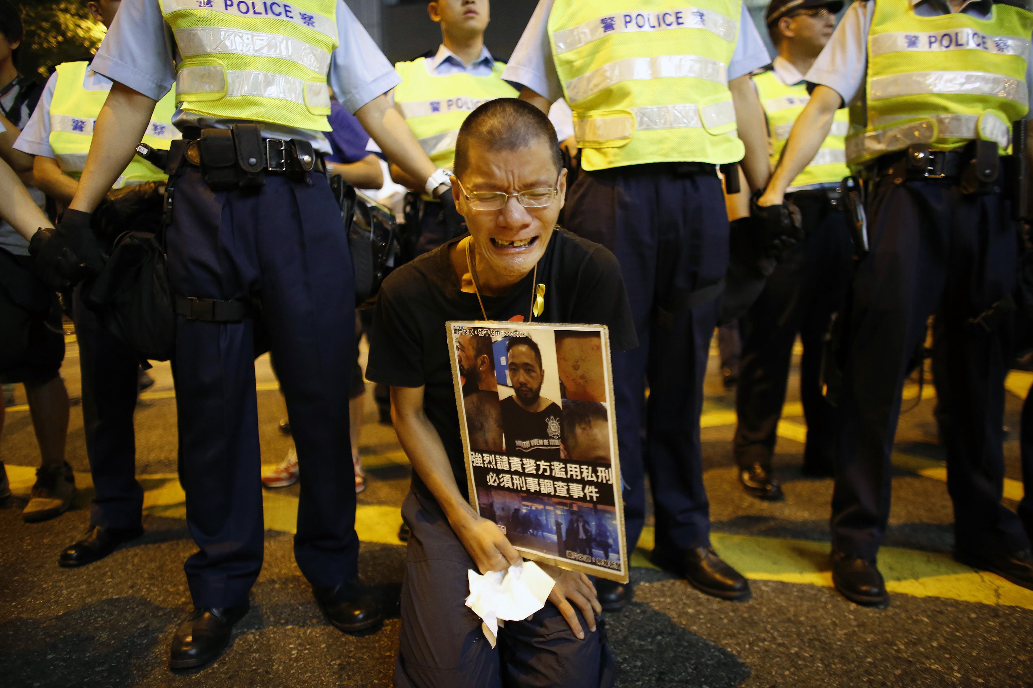 Người đàn ông cầm bức ảnh miêu tả Tằng Giang, thành viên của Đảng Dân sự bị các nhân viên cảnh sát mặc thường phục đánh đập tại khu vực biểu tình chính ở huyện Admiralty, Hồng Kông vào ngày 23/10/2014. Sau cuộc điều tra, 7 nhân viên an ninh tham gia đánh đập đã bị bắt vào hôm 26/11. (Ảnh: Internet)