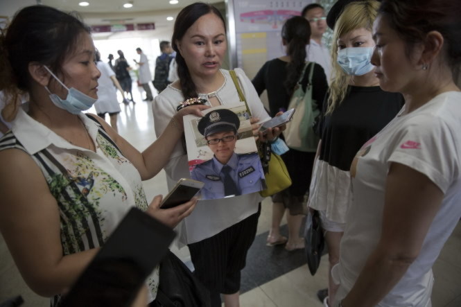 Bà Zhang Yibi (bìa trái) đến các bệnh viện đưa hình con trai mình là Lei Chi, một lính cứu hỏa 21 tuổi bị mất tích sau khi tham gia cứu chữa trong vụ nổ ở Thiên Tân - Ảnh: Reuters