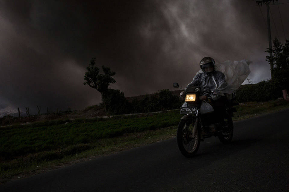 Người đàn ông trên chiếc xe máy khi núi Sinabung phun tro, nhìn từ làng Tiga Kicat ngày 20 tháng 06 năm 2015